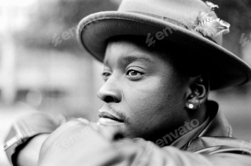 Preview: Monochrome portrait of man wearing a hat and looking pensive outdoors.