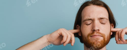 Preview: Young ginger man with beard plugging his ears while posing on camera