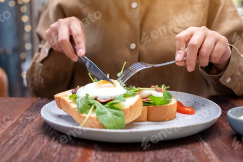 Preview: A woman eating breakfast sandwich with eggs, bacon and sour cream by knife and spoon