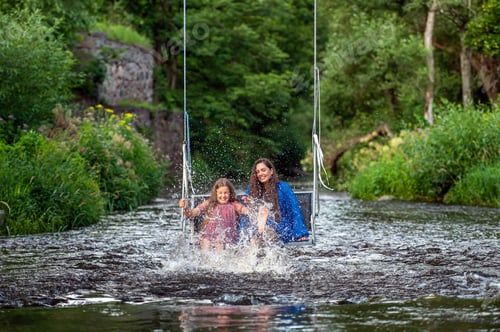 Preview: a woman and a young girl are swinging across a fast-flowing river, laughing and splashing with water