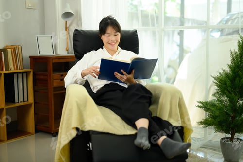 Preview: Relaxed young woman reading a book on a comfortable armchair