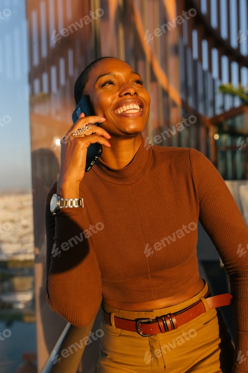 Preview: Joyful ethnic businesswoman having phone call near window in skyscraper
