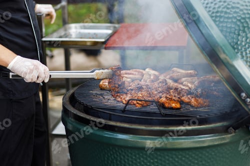Preview: Chef cooking delicious bbq meat in grill at street market in city. Vendor roasting steak at festival
