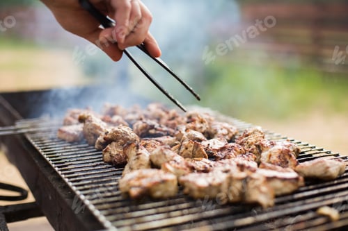 Preview: A man prepares meat on the grill, close-up photo. Grilled meat is smoking