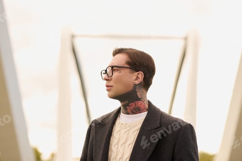Preview: Stylish young man with tattoos exudes confidence in a modern urban setting during golden hour