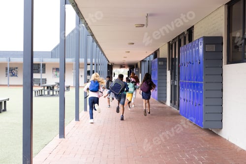 Preview: Rear view of diverse children with schoolbags running in elementary school corridor, copy space
