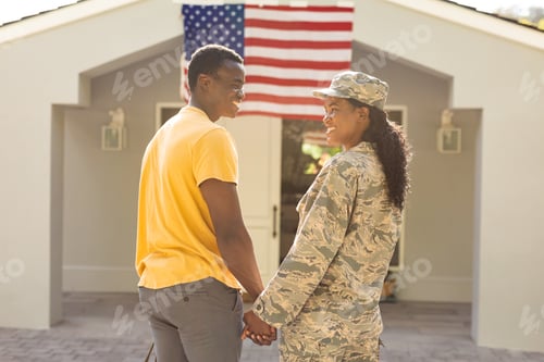 Preview: Happy female mid adult african american soldier holding hand of husband on arrival at home