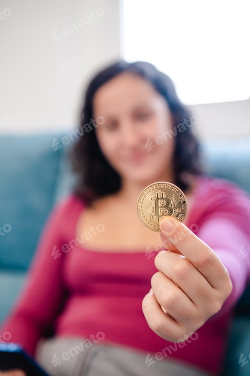 Preview: Unfocussed and unrecognized young woman with a bitcoin coin in her hand at home