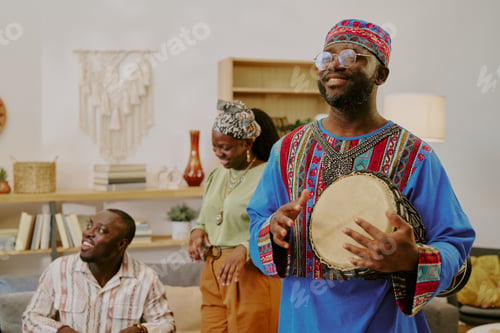 Preview: Young Black Man Playing Drum While Friends Celebrate Kwanzaa Indoors