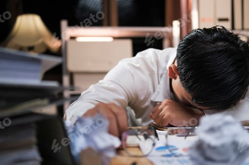 Preview: Young tired businessman lying on table at night office.