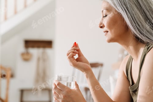 Preview: Mature asian woman taking her medication while sitting on couch