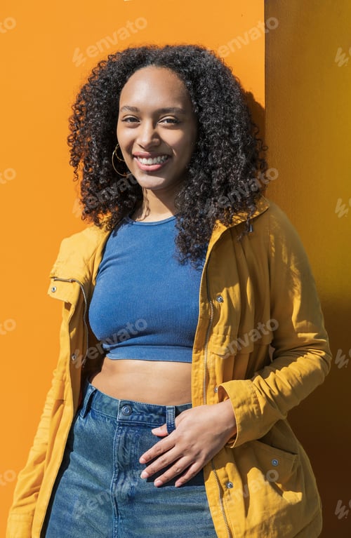 Preview: Confident smiling latina woman posing against bold orange wall