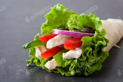 Preview: Chicken caesar salad wrap with lettuce, red onion, red bell pepper and cucumber on slate surface