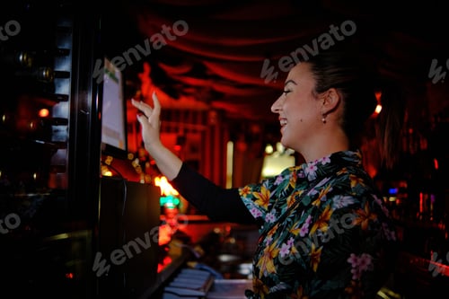 Preview: Female waitress using a touch screen computer and smiling while works behind the counter in a bar.