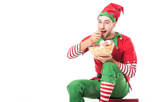 Preview: man in christmas elf costume eating popcorn and looking at camera isolated on white
