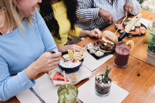 Preview: Young multiracial friends having breakfast outdoors in restaurant - Focus on right girl hand