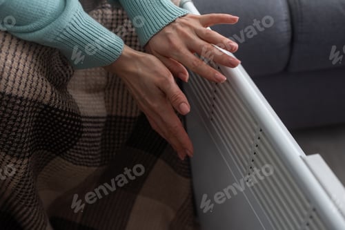 Preview: Woman warming hands near heater indoors, closeup