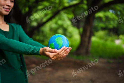 Preview: An Asian woman holds a globe in green forest,symbolizing importance preserving nature.emphasizes