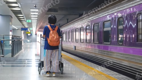 Preview: Rear view of Asian female passenger with luggage trolley on platform at train station