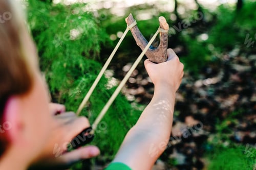 Preview: Boy enjoying his summer vacation throwing rocks with a slingshot in a forest.