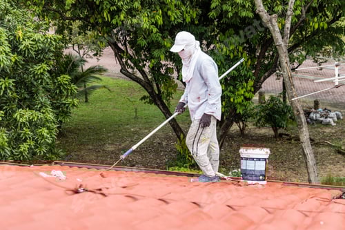 Preview: Worker painting red rooftop with roller at residential building during renovation