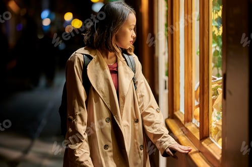 Preview: Young woman looking at a shop window at night