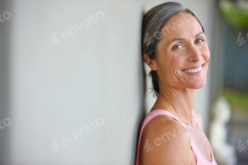 Preview: Portrait of an attractive mature woman in gymwear leaning against a gray wall