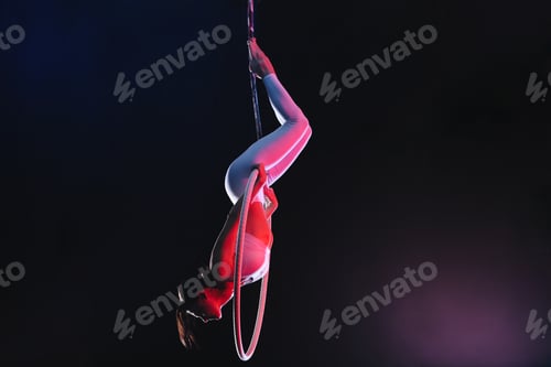 Preview: Young woman performing acrobatic element on aerial ring against dark background