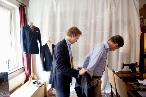 Preview: Side view of tailor assisting man for wearing suit
