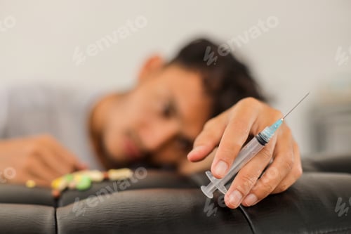 Preview: Close Up Of Hand Holding Syringe Addicted To Drugs Against Depressed Man Background