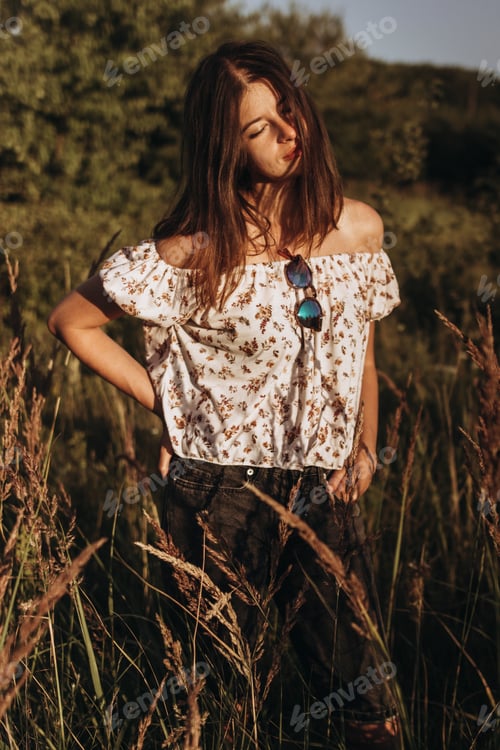 Preview: stylish hipster woman walking in wildflowers in summer evening field