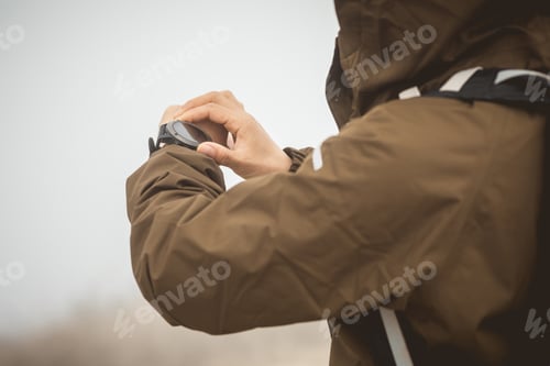 Preview: Woman hiker checking the altitude on her smartwatch at foggy mountain top