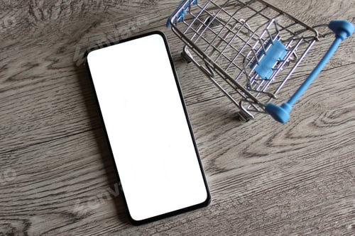 Preview: Smartphone with blank white screen inside shopping trolley with copy space