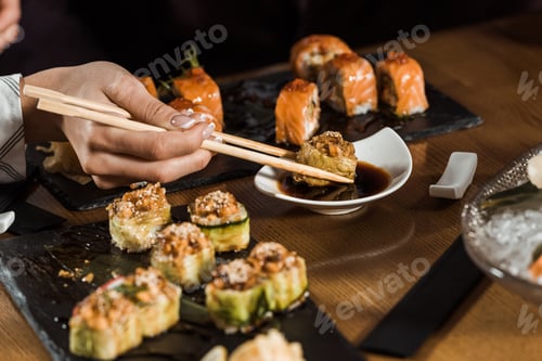 Preview: Partial view of woman dipping sushi in soy sauce with chopsticks