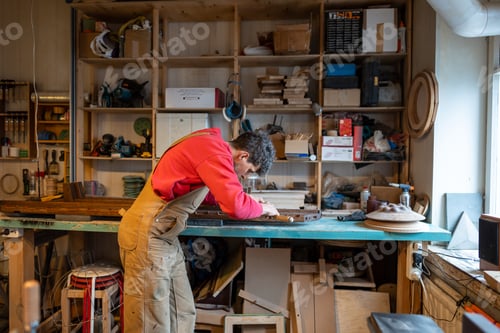 Preview: Focused male carpenter use chisel works with wooden piece of handmade furniture in joinery workshop.
