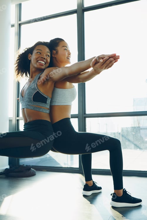 Preview: Two young women exercising in gym, doing squats, back to back