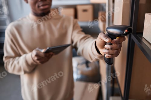 Preview: Focus on hand of young man holding scanner by one of boxes on shelf