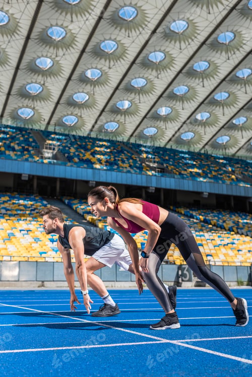 Preview: fit young male and female sprinters in start position on running track at sports stadium