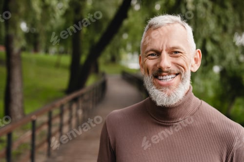 Preview: Smiling with toothy smile caucasian handsome mature man looking at the camera while walking