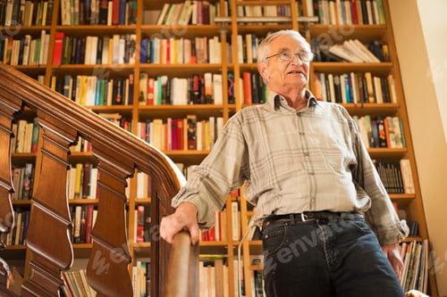Preview: Elderly man standing on wooden staircase surrounded by books