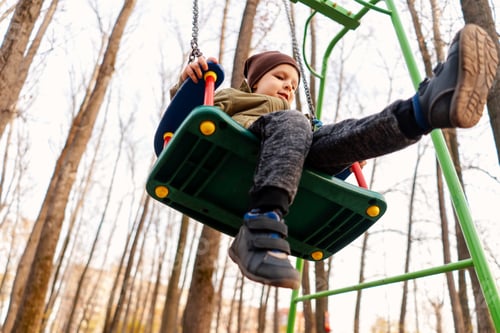 Preview: A young toddler boy swinging on a swing in forest. Bottom view.