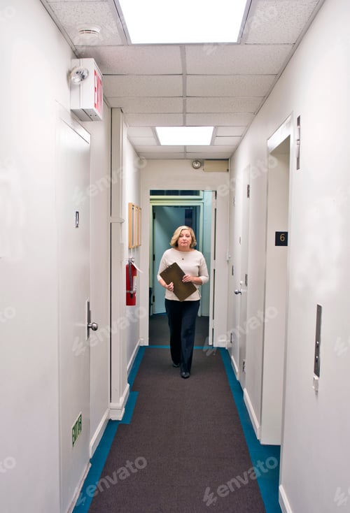Preview: Business professional carrying documents in an office hallway.