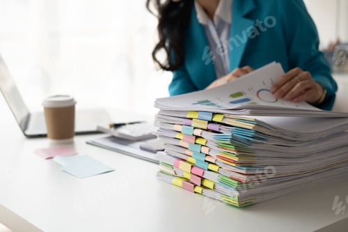 Preview: Young professional businesswoman working with stack of papers, searshing for the right file to work