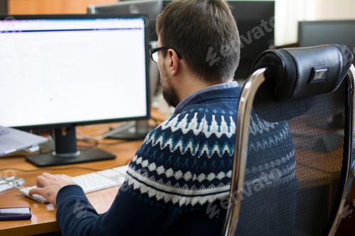 Preview: Young programmer typing on a freestanding white keyboard on a wooden table in front of two monitors