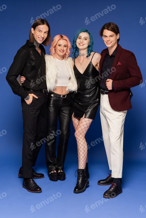 Preview: full length of joyful nonbinary friends in stylish clothes smiling at camera on blue
