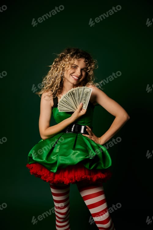 Preview: smiley curly elf in green new year dress and striped stockings holding cash with one arm akimbo