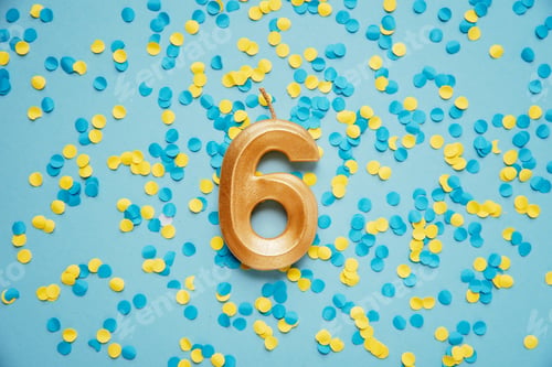 Preview: Number 6 six golden celebration birthday candle on yellow and blue confetti Background.