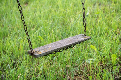 Preview: Empty wooden board chain swing, hanging above green lawn in backyard of abandoned house.