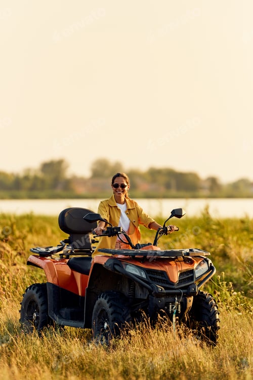 Preview: Portrait of a smiling woman driving a rented quad bike, with sunglasses on.