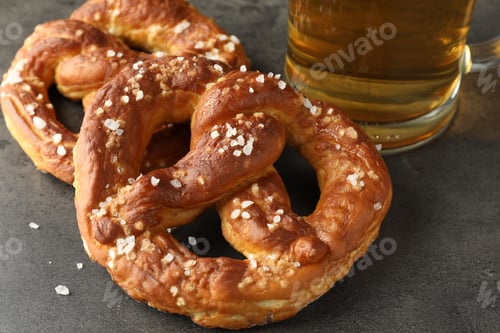 Preview: Tasty pretzels and glass of beer on dark textured table, closeup